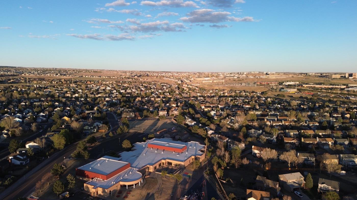 Golden-hour aerial sweeping over suburban rooftops
