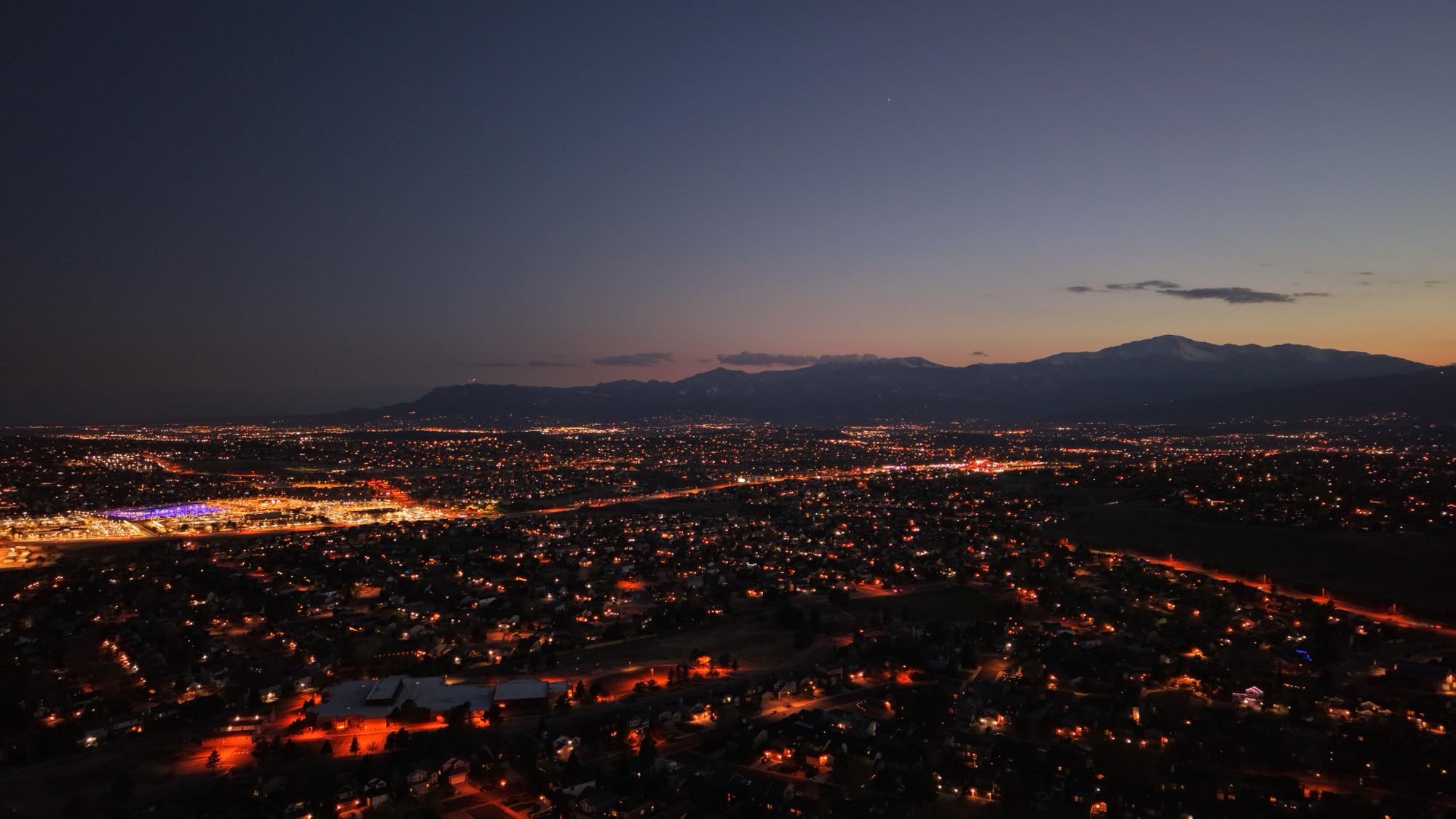 Aerial dusk view of a city skyline beneath the Rocky Mountains, captured by RHYNO DRONE