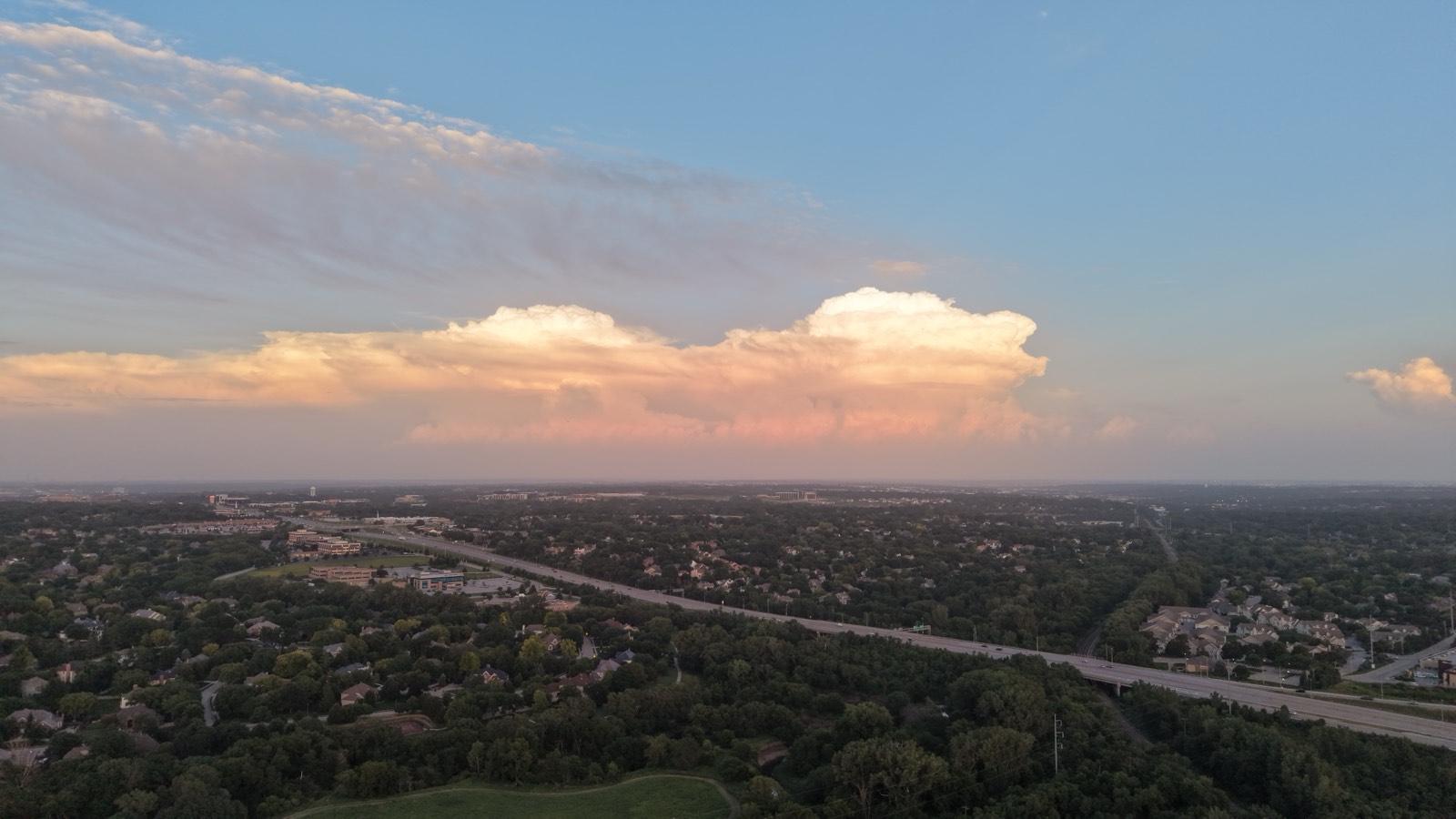 Aerial of suburban sprawl beneath a towering sunset thunderhead on the horizon